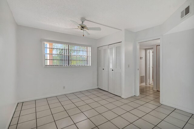 unfurnished bedroom with ceiling fan, a closet, light tile patterned flooring, and a textured ceiling