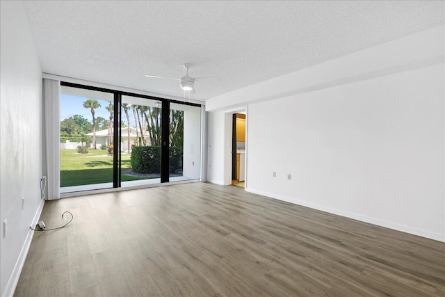 unfurnished room with a textured ceiling, baseboards, a wall of windows, and wood finished floors