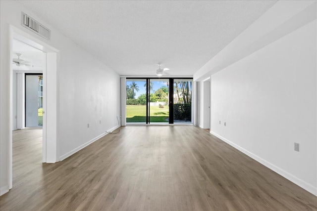 spare room featuring expansive windows, wood finished floors, visible vents, and baseboards