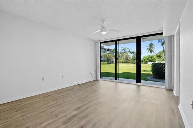 unfurnished room featuring baseboards, a ceiling fan, light wood-style flooring, expansive windows, and a textured ceiling