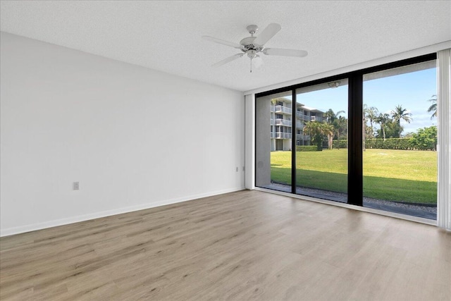 spare room featuring a textured ceiling, wood finished floors, a ceiling fan, baseboards, and floor to ceiling windows