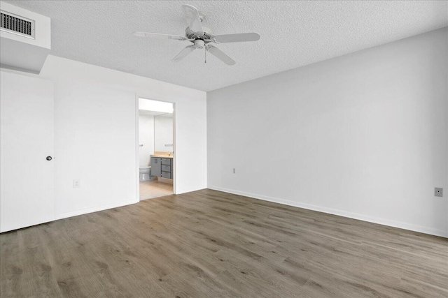 unfurnished bedroom with baseboards, visible vents, connected bathroom, wood finished floors, and a textured ceiling