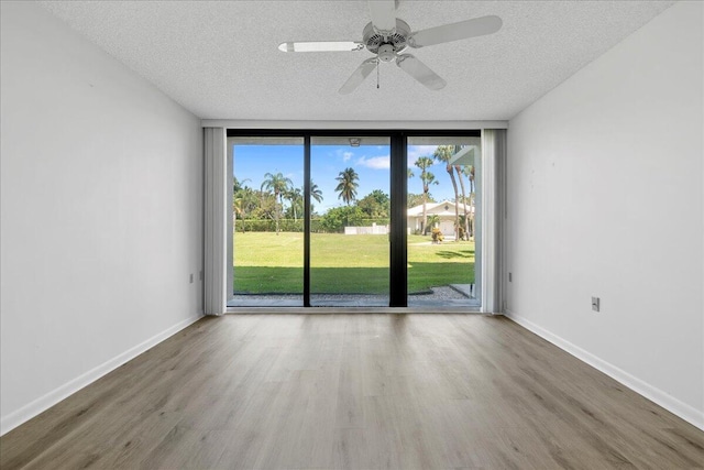 unfurnished room featuring a textured ceiling, a wall of windows, wood finished floors, and baseboards