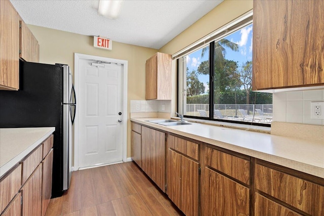 kitchen featuring dark wood-style flooring, light countertops, decorative backsplash, freestanding refrigerator, and a sink