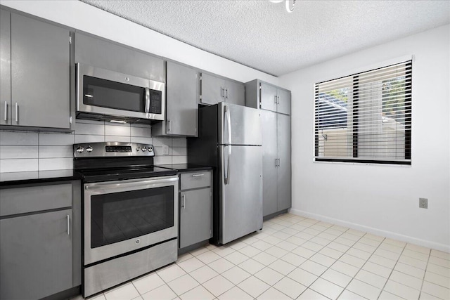 kitchen with a textured ceiling, appliances with stainless steel finishes, backsplash, gray cabinets, and dark countertops