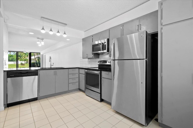 kitchen featuring decorative backsplash, dark countertops, gray cabinets, stainless steel appliances, and a sink