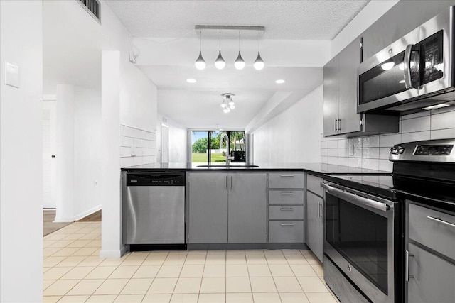 kitchen featuring gray cabinetry, stainless steel appliances, a sink, decorative backsplash, and dark countertops