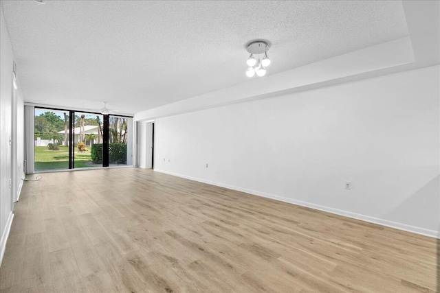 empty room featuring light wood finished floors, expansive windows, baseboards, and a textured ceiling