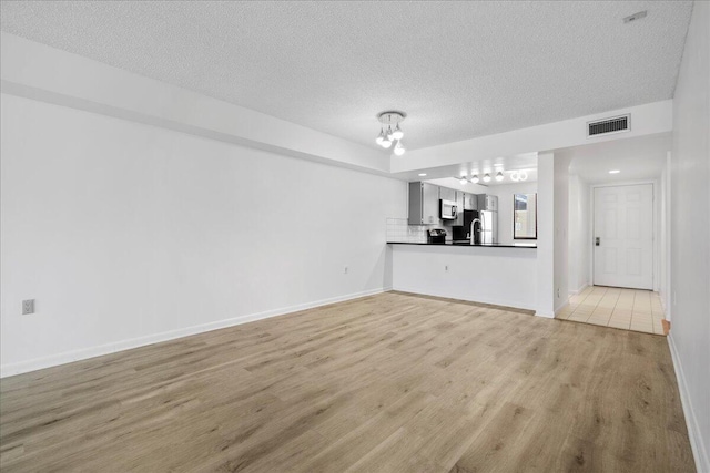 unfurnished living room featuring light wood-style floors, visible vents, a textured ceiling, and baseboards