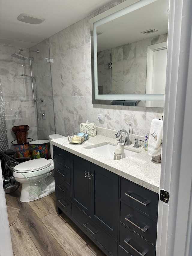 bathroom with vanity, toilet, tiled shower, and tile walls