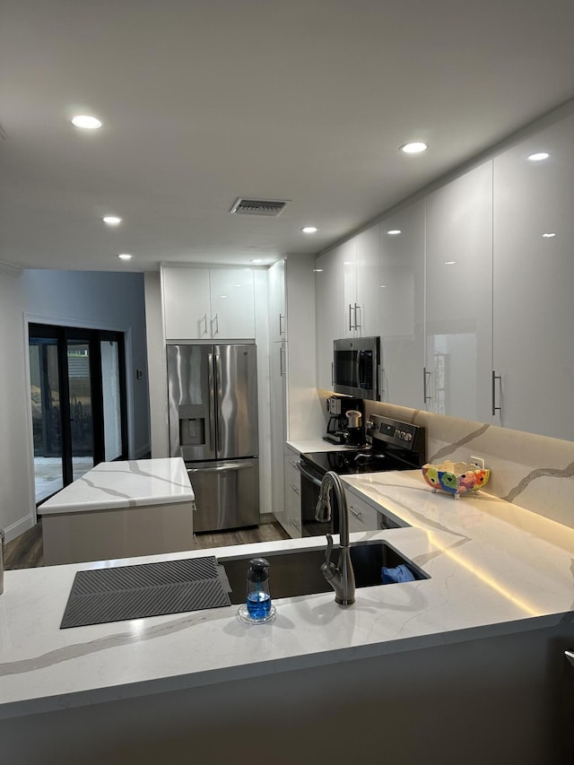 kitchen featuring kitchen peninsula, light stone counters, white cabinets, and stainless steel appliances