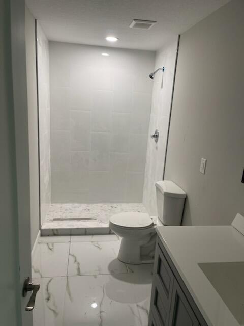 bathroom featuring tiled shower, vanity, and toilet