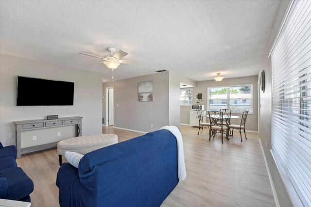 living room featuring a textured ceiling, ceiling fan, and light hardwood / wood-style flooring