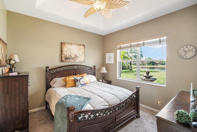 bedroom with ceiling fan, light colored carpet, and a tray ceiling