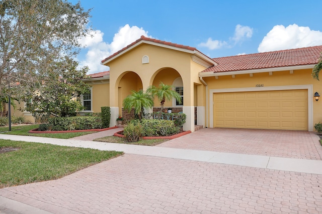 mediterranean / spanish home featuring a garage, decorative driveway, a tiled roof, and stucco siding