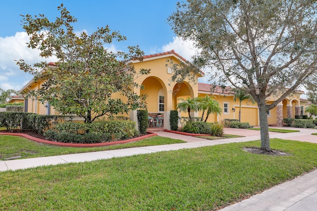 mediterranean / spanish-style house with a front yard, a tile roof, and stucco siding