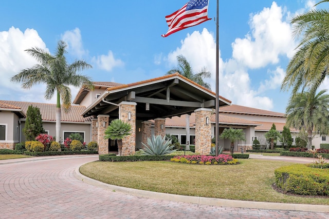 view of front facade with stone siding, a front yard, a tiled roof, and stucco siding