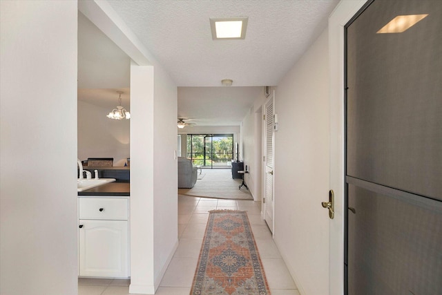 corridor featuring light tile patterned flooring, a textured ceiling, and a notable chandelier