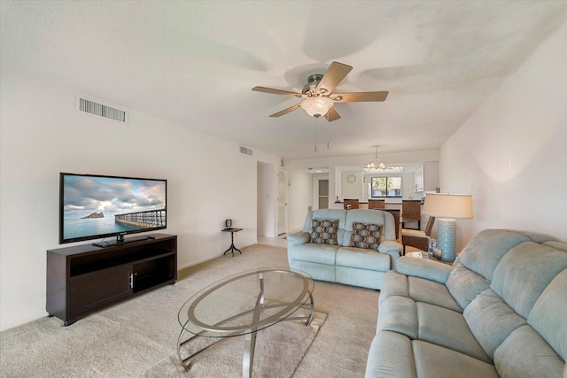 living room with a textured ceiling, ceiling fan with notable chandelier, and light colored carpet