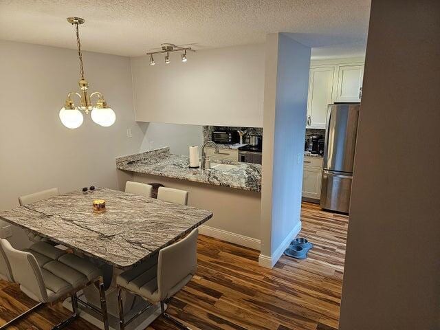 kitchen featuring a kitchen bar, stainless steel fridge, kitchen peninsula, pendant lighting, and a chandelier