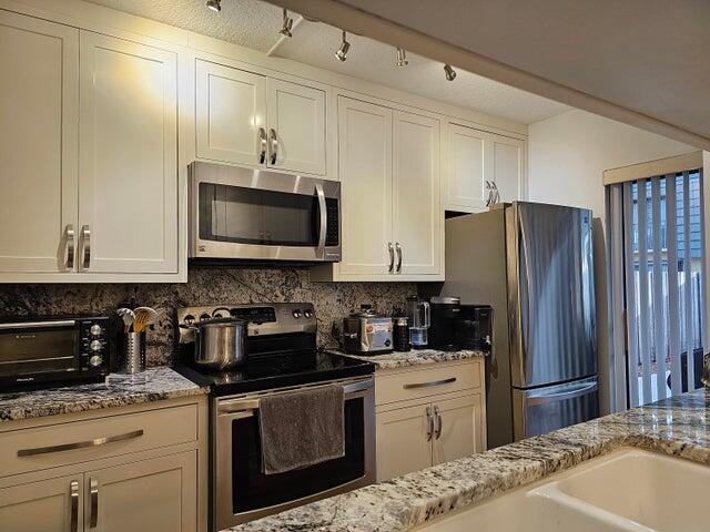 kitchen with light stone countertops, decorative backsplash, stainless steel appliances, and white cabinetry