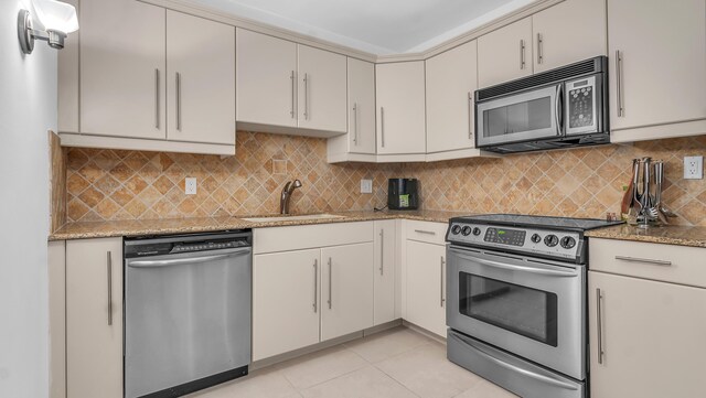 kitchen with backsplash, appliances with stainless steel finishes, sink, and light stone countertops