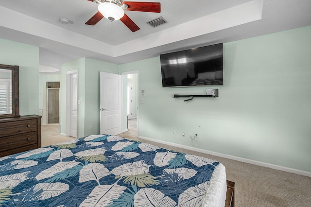 carpeted bedroom featuring a tray ceiling, ensuite bath, and ceiling fan