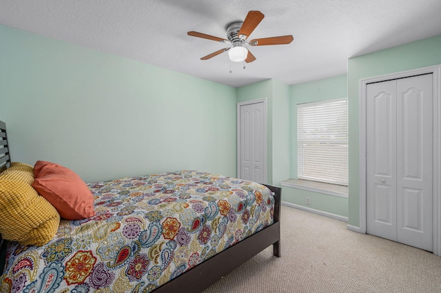 carpeted bedroom with ceiling fan, a textured ceiling, and two closets