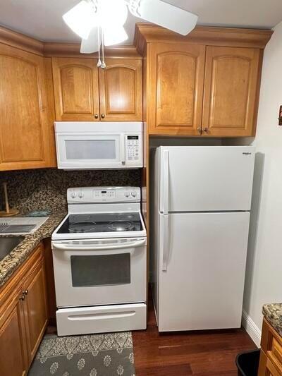 kitchen featuring decorative backsplash, dark hardwood / wood-style flooring, dark stone counters, and white appliances