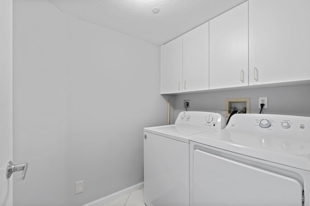 laundry room featuring cabinets, light tile patterned floors, a textured ceiling, and separate washer and dryer