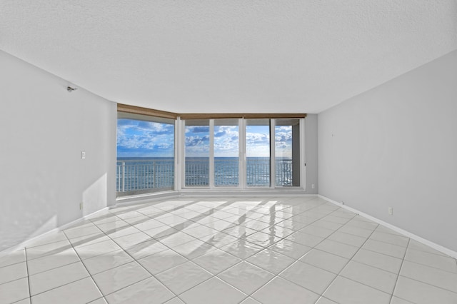 empty room with light tile patterned flooring, a textured ceiling, and a wall of windows