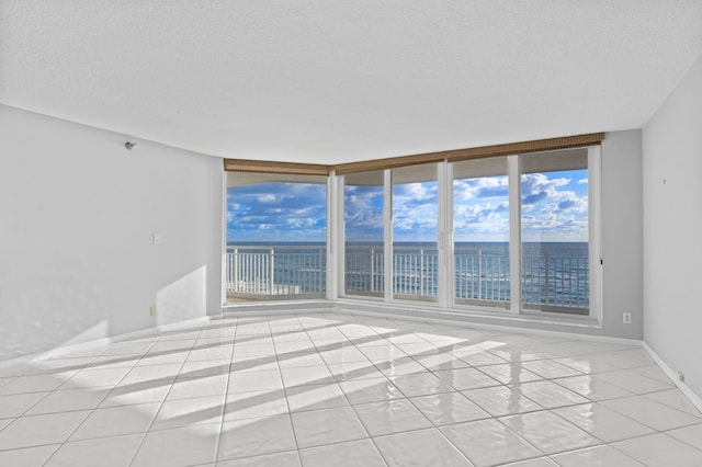 unfurnished room featuring a textured ceiling, a water view, a wall of windows, and light tile patterned flooring