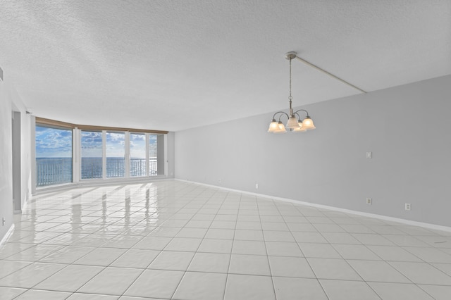 tiled empty room with a textured ceiling, a notable chandelier, and a wall of windows