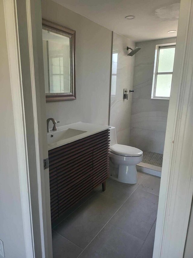 bathroom featuring tile patterned flooring, vanity, toilet, and a tile shower