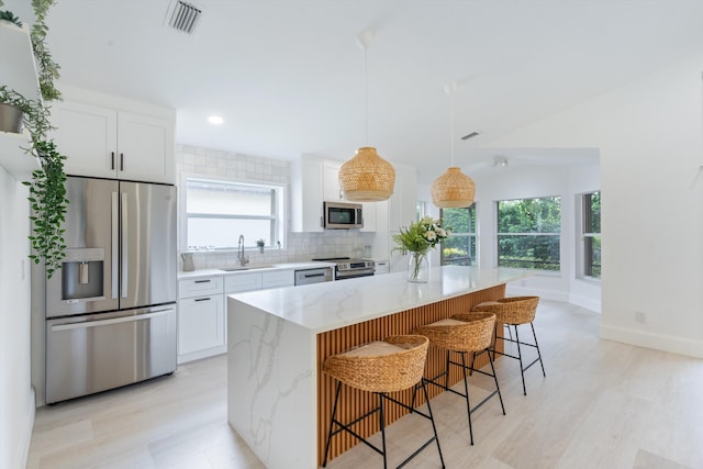 kitchen with white cabinetry, a center island, sink, stainless steel appliances, and light stone counters