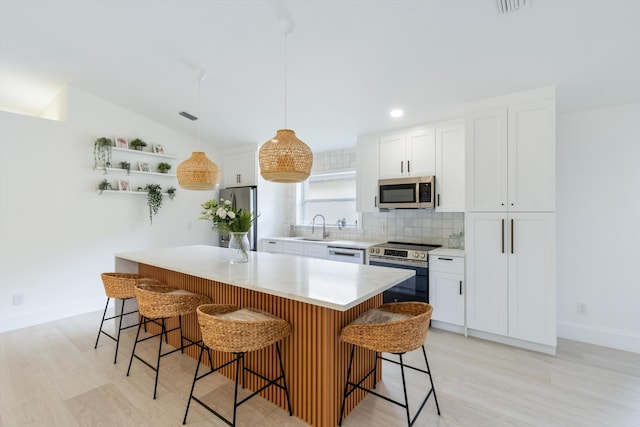 kitchen featuring white cabinets, a kitchen island, hanging light fixtures, and appliances with stainless steel finishes