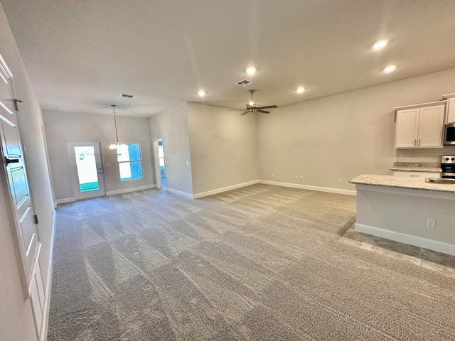 unfurnished living room with ceiling fan with notable chandelier, light colored carpet, and sink