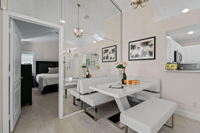 dining area with ceiling fan with notable chandelier, light wood-type flooring, crown molding, and lofted ceiling