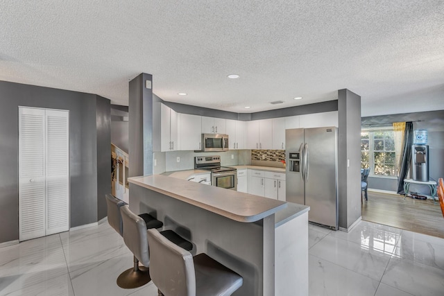 kitchen featuring kitchen peninsula, a textured ceiling, a breakfast bar area, white cabinets, and appliances with stainless steel finishes