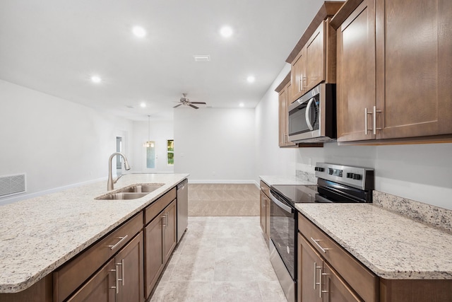 kitchen with a kitchen island with sink, sink, ceiling fan, light stone countertops, and appliances with stainless steel finishes