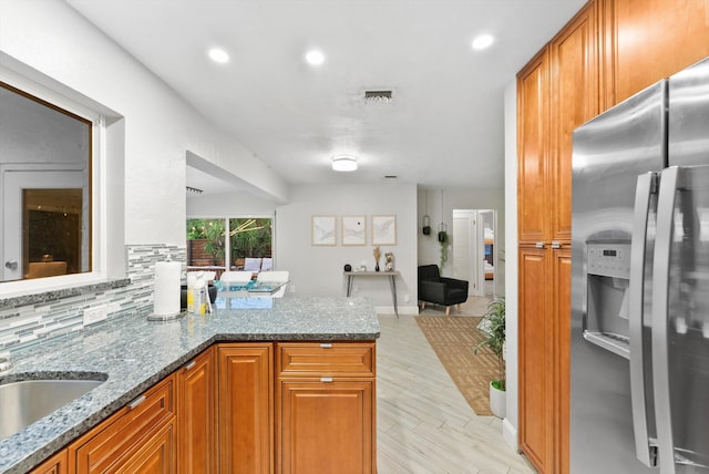 kitchen with light hardwood / wood-style floors, stainless steel fridge, dark stone counters, kitchen peninsula, and backsplash