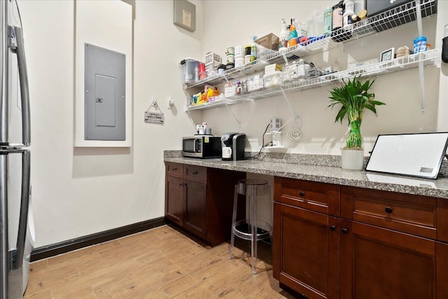 bar with light stone countertops, light wood-type flooring, electric panel, and stainless steel appliances