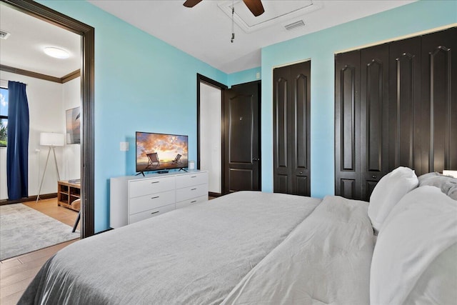 bedroom with ceiling fan, light wood-type flooring, crown molding, and two closets