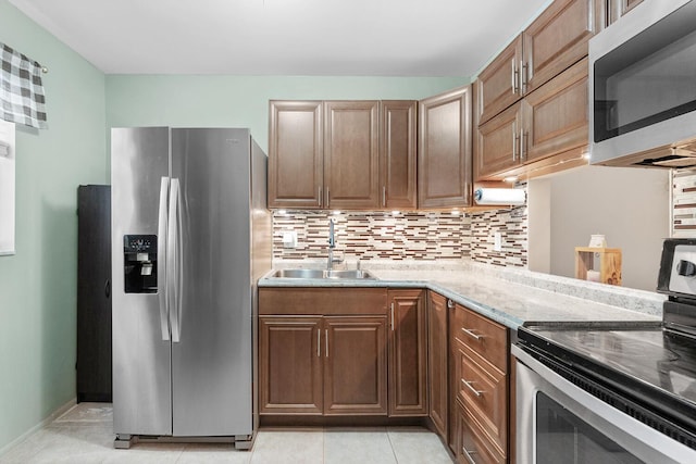 kitchen featuring light stone countertops, appliances with stainless steel finishes, tasteful backsplash, sink, and light tile patterned floors