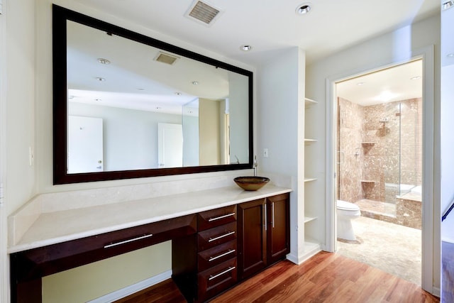 bathroom featuring toilet, hardwood / wood-style floors, tiled shower, and vanity