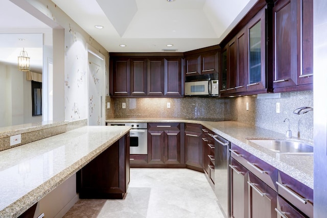 kitchen featuring a raised ceiling, light stone countertops, sink, and stainless steel appliances