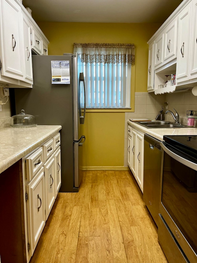 kitchen featuring white cabinetry, stainless steel appliances, decorative backsplash, sink, and light hardwood / wood-style floors