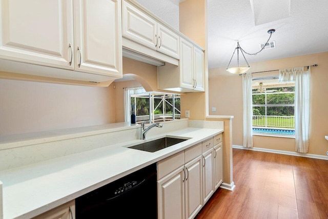 kitchen with hanging light fixtures, sink, black dishwasher, and light hardwood / wood-style floors