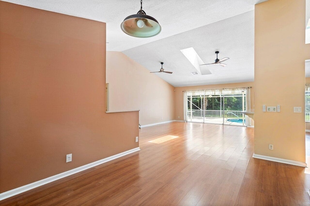 empty room with wood-type flooring, a textured ceiling, vaulted ceiling with skylight, and ceiling fan