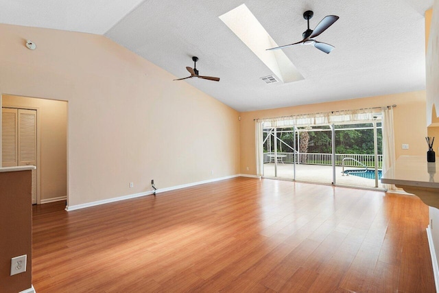 unfurnished living room with a textured ceiling, wood-type flooring, lofted ceiling with skylight, and ceiling fan